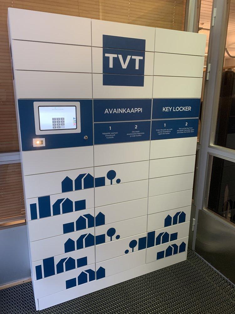 TVT:n avainhallinta-automaatti, jossa on valkoinen pohja ja sinisellä teipattuna asuntojen kuvia.
