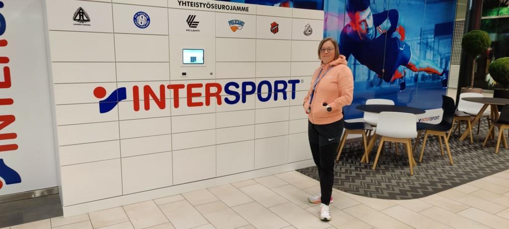 Intersport Karisman kauppias Terhi Kokko seisoo valkoisen Smartbox pakettiautomaatin edessä.